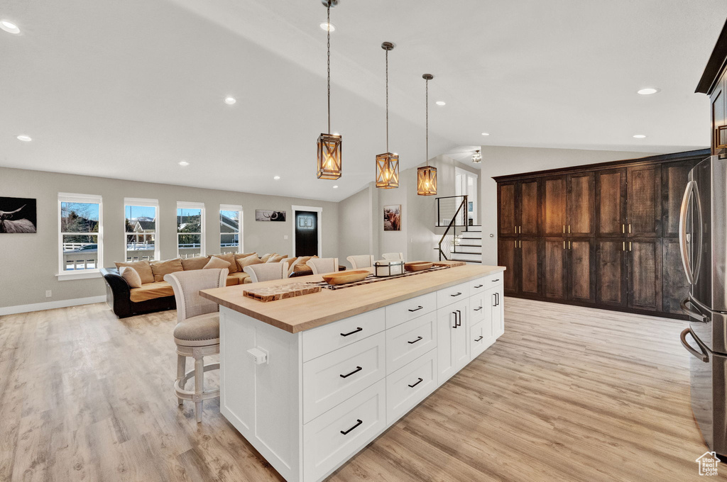 Kitchen with light wood-type flooring, pendant lighting, white cabinetry, a kitchen island, and wooden counters