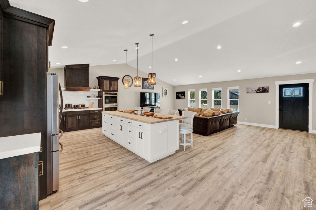 Kitchen with light wood-type flooring, tasteful backsplash, appliances with stainless steel finishes, lofted ceiling, and a center island