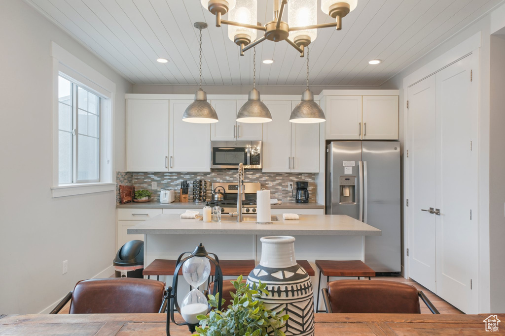 Kitchen featuring white cabinets, hanging light fixtures, appliances with stainless steel finishes, and a healthy amount of sunlight