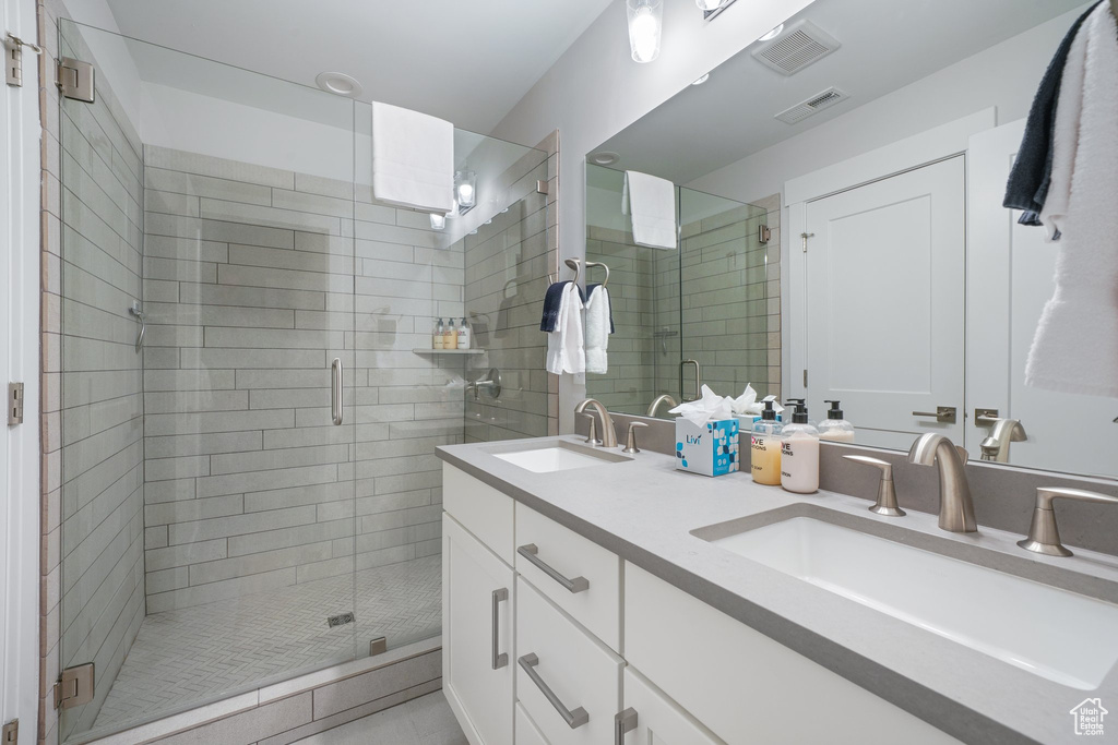 Bathroom featuring a shower with door, double sink, and vanity with extensive cabinet space