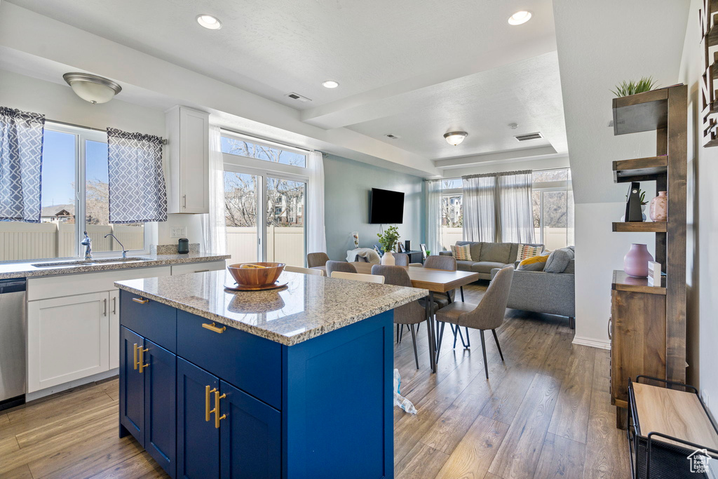 Kitchen featuring sink, white cabinets, blue cabinetry, light stone countertops, and light wood-type flooring