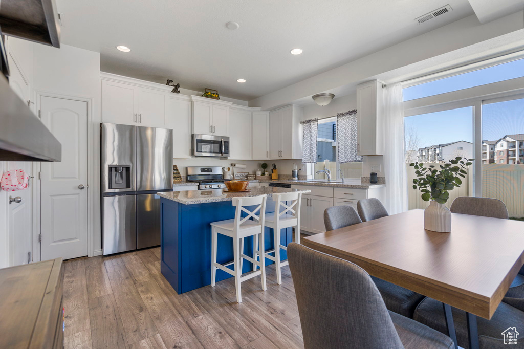 Kitchen featuring a kitchen island, light hardwood / wood-style flooring, a breakfast bar area, stainless steel appliances, and white cabinetry