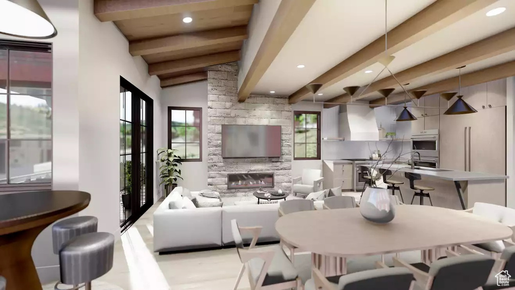 Dining space with lofted ceiling with beams, light hardwood / wood-style flooring, a stone fireplace, and a healthy amount of sunlight