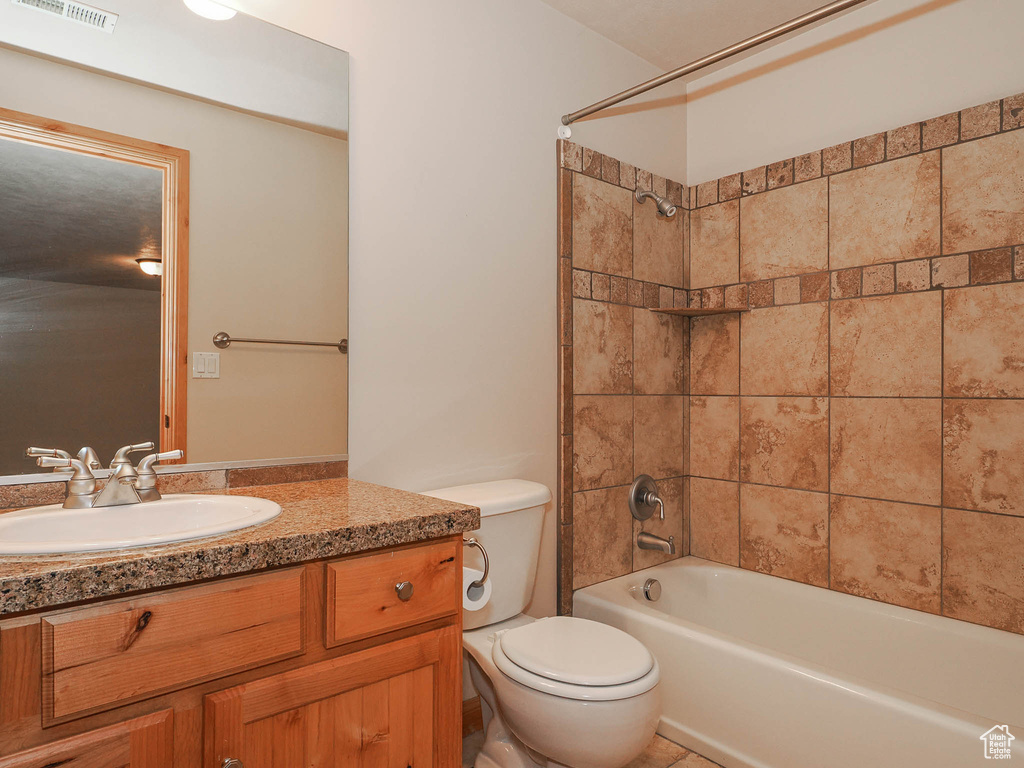Full bathroom with tiled shower / bath combo, toilet, and large vanity