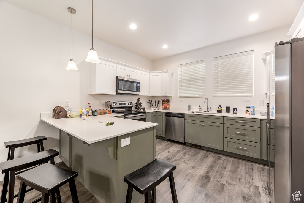 Kitchen with pendant lighting, stainless steel appliances, a breakfast bar, light hardwood / wood-style flooring, and sink