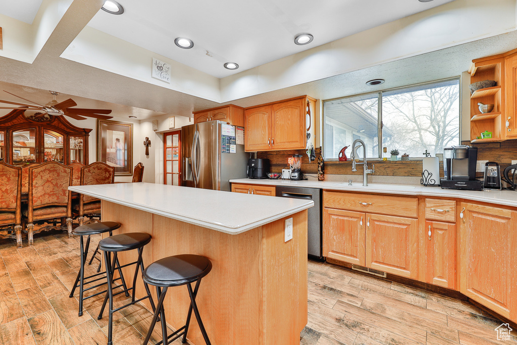 Kitchen featuring ceiling fan, light wood-type flooring, a center island, a breakfast bar area, and stainless steel appliances