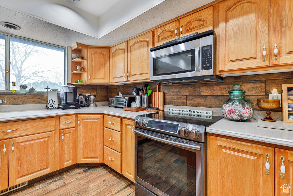 Kitchen with appliances with stainless steel finishes, light wood-type flooring, sink, and backsplash