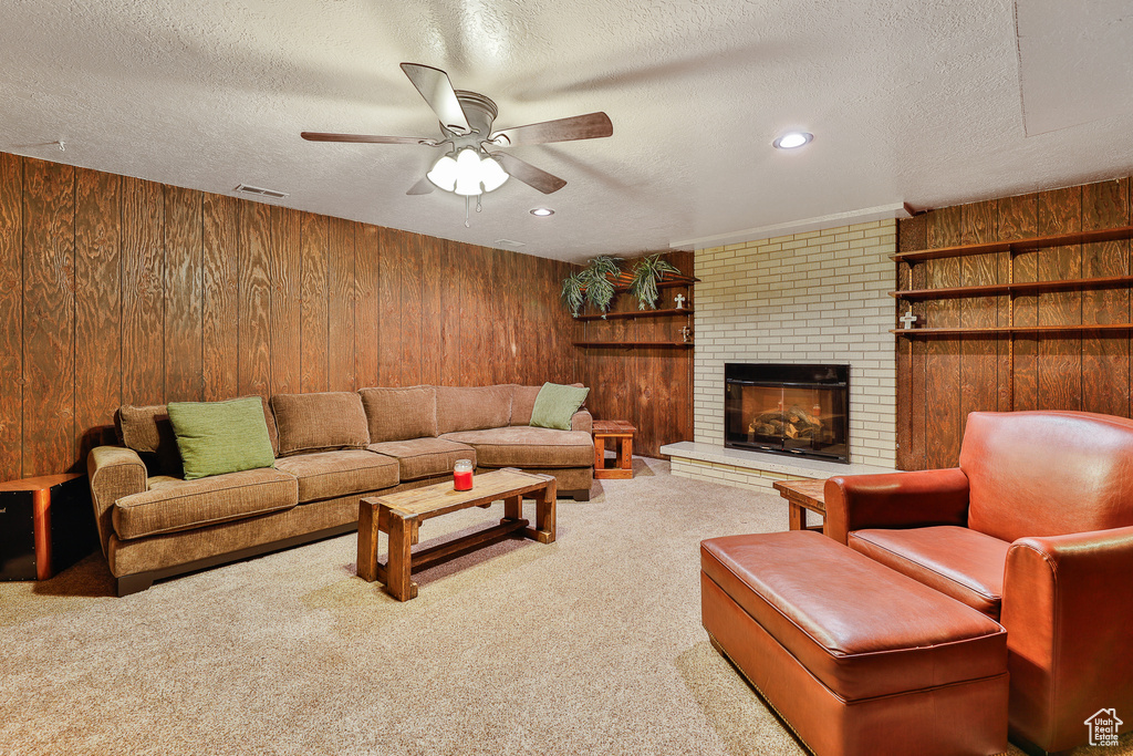 Living room featuring a brick fireplace, wood walls, a textured ceiling, and ceiling fan