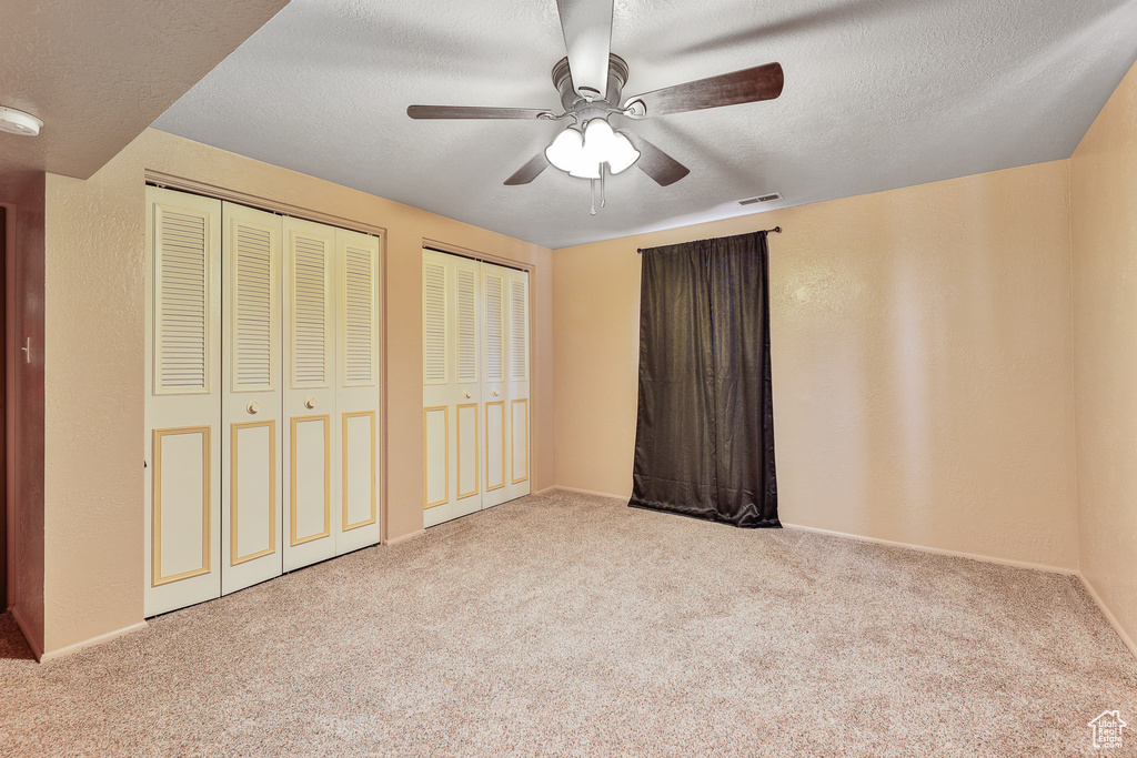 Unfurnished bedroom featuring two closets, light carpet, a textured ceiling, and ceiling fan