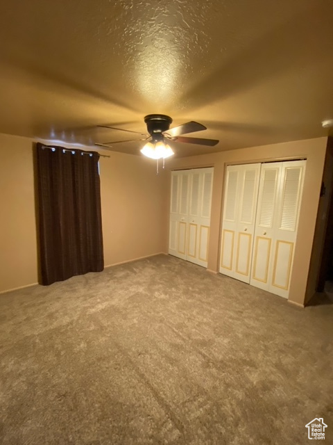Unfurnished bedroom featuring ceiling fan, light colored carpet, and two closets