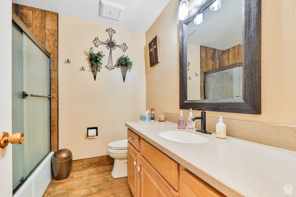Full bathroom with vanity, toilet, hardwood / wood-style flooring, and shower / bath combination with glass door