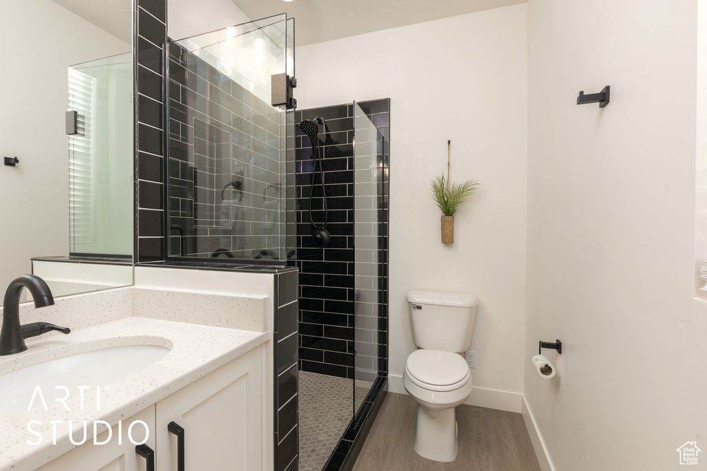 Bathroom with hardwood / wood-style floors, large vanity, tiled shower, and toilet