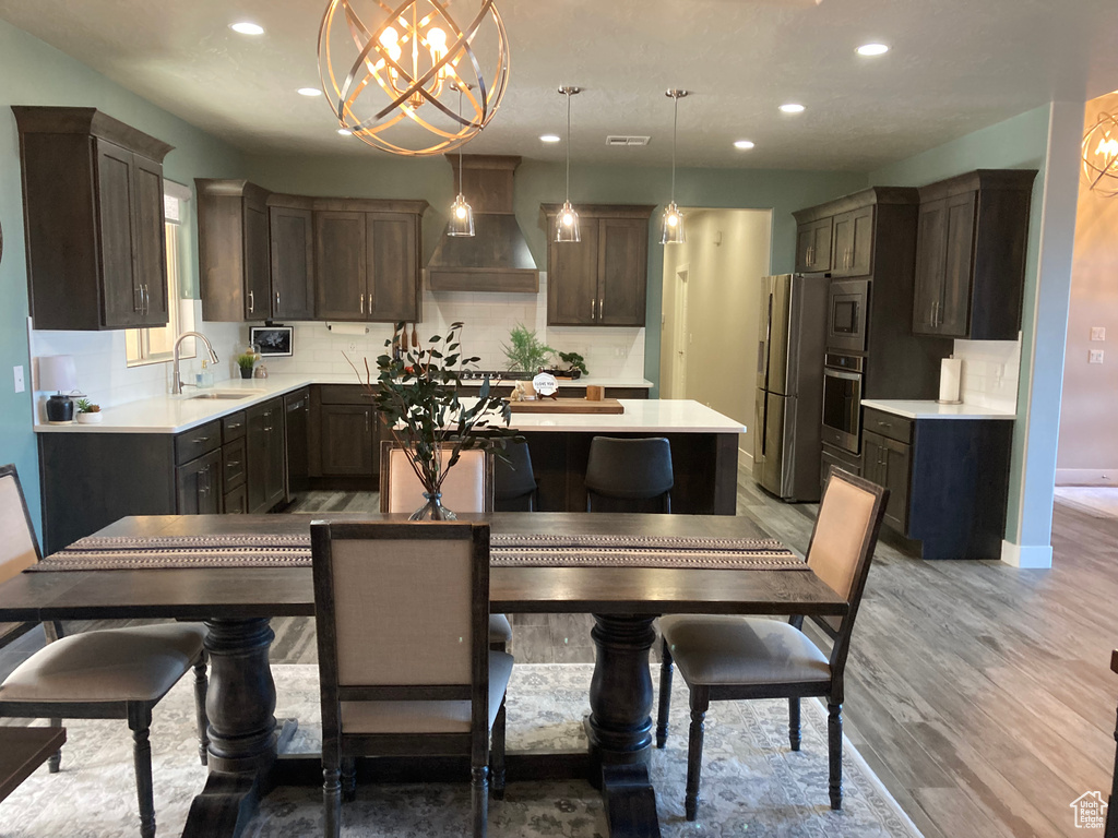 Kitchen with an inviting chandelier, stainless steel appliances, custom range hood, hanging light fixtures, and light hardwood / wood-style floors