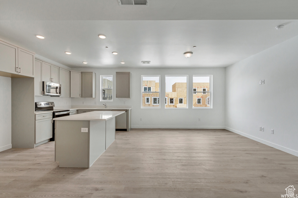 Kitchen with appliances with stainless steel finishes, gray cabinets, a center island, and light hardwood / wood-style flooring