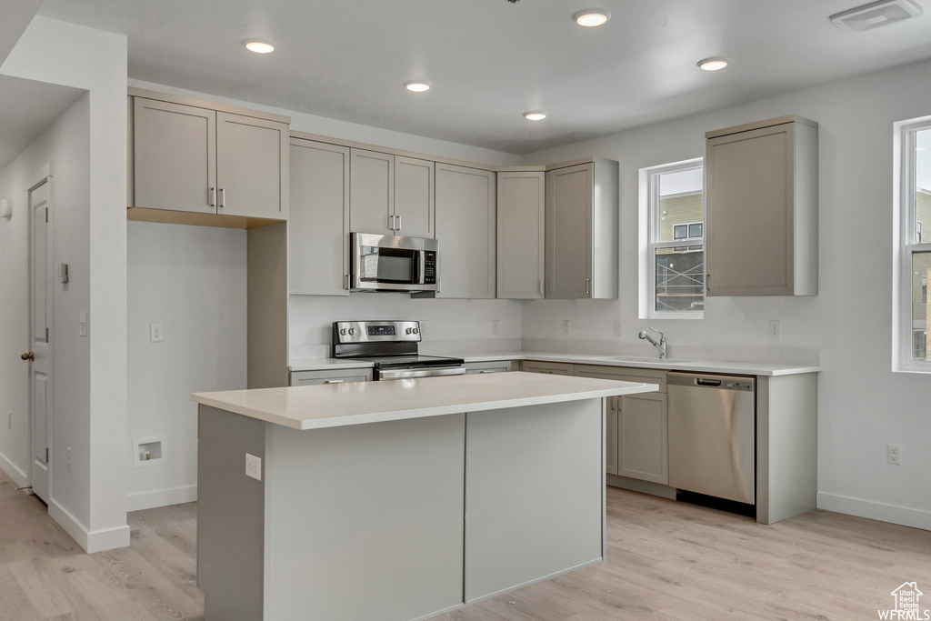 Kitchen featuring stainless steel appliances, a kitchen island, gray cabinets, and light hardwood / wood-style flooring