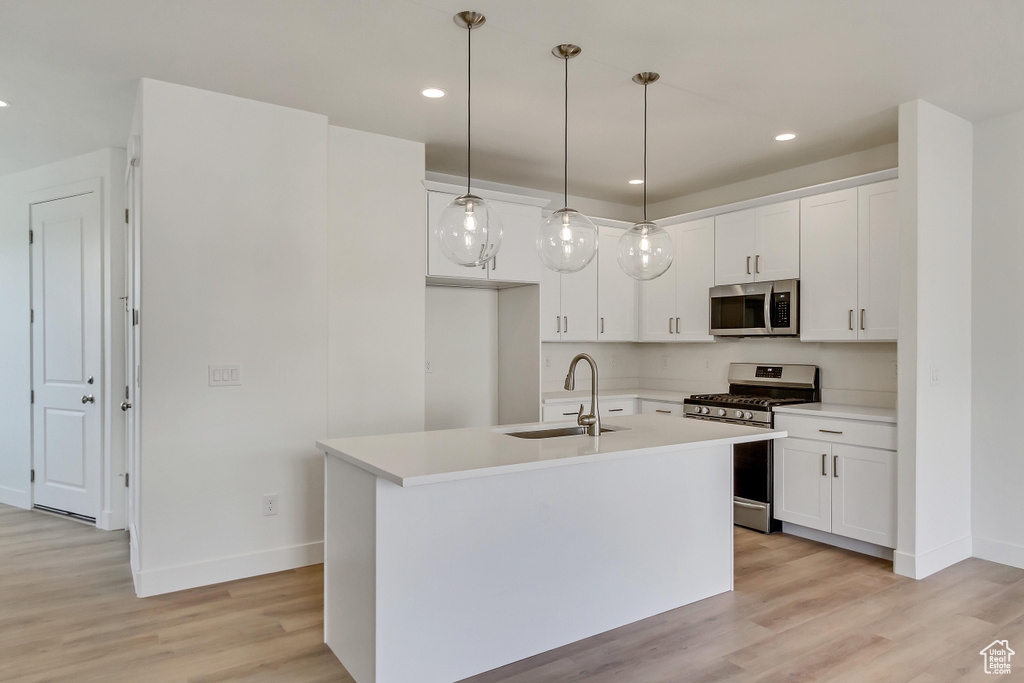 Kitchen featuring a center island with sink, light wood-type flooring, white cabinets, hanging light fixtures, and stainless steel appliances