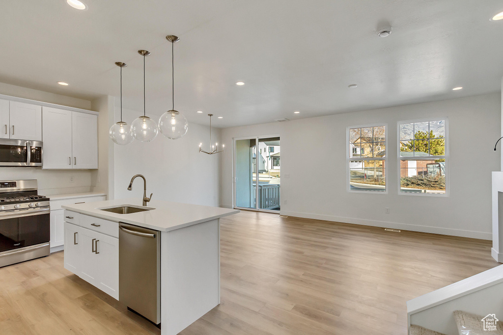 Kitchen featuring white cabinetry, an island with sink, stainless steel appliances, and light wood-type flooring