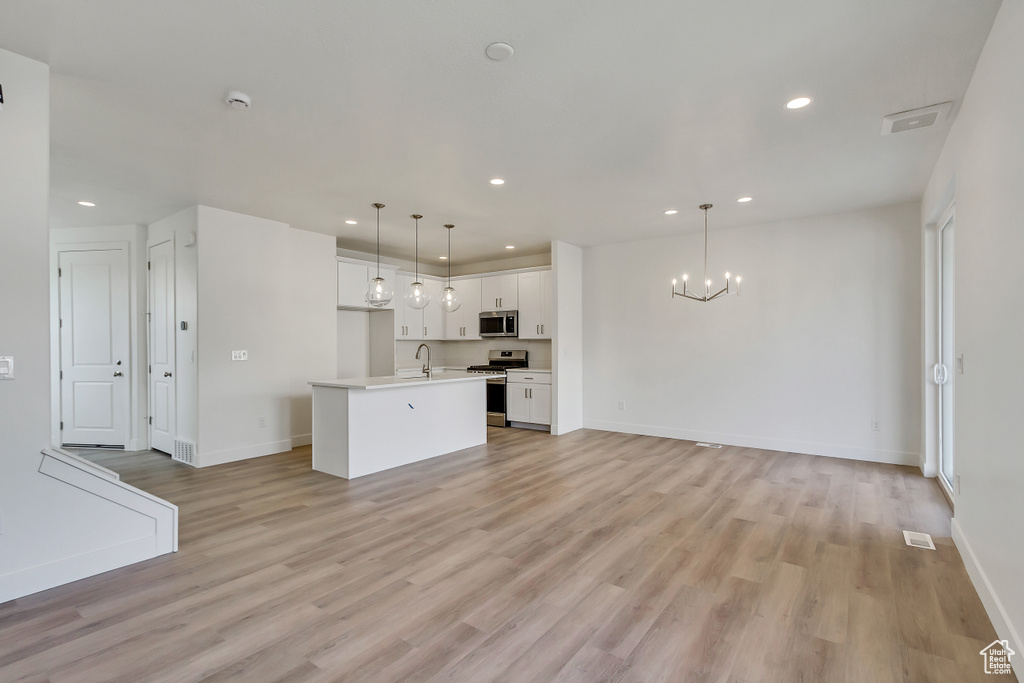 Kitchen featuring light hardwood / wood-style flooring, a kitchen island with sink, white cabinets, pendant lighting, and appliances with stainless steel finishes