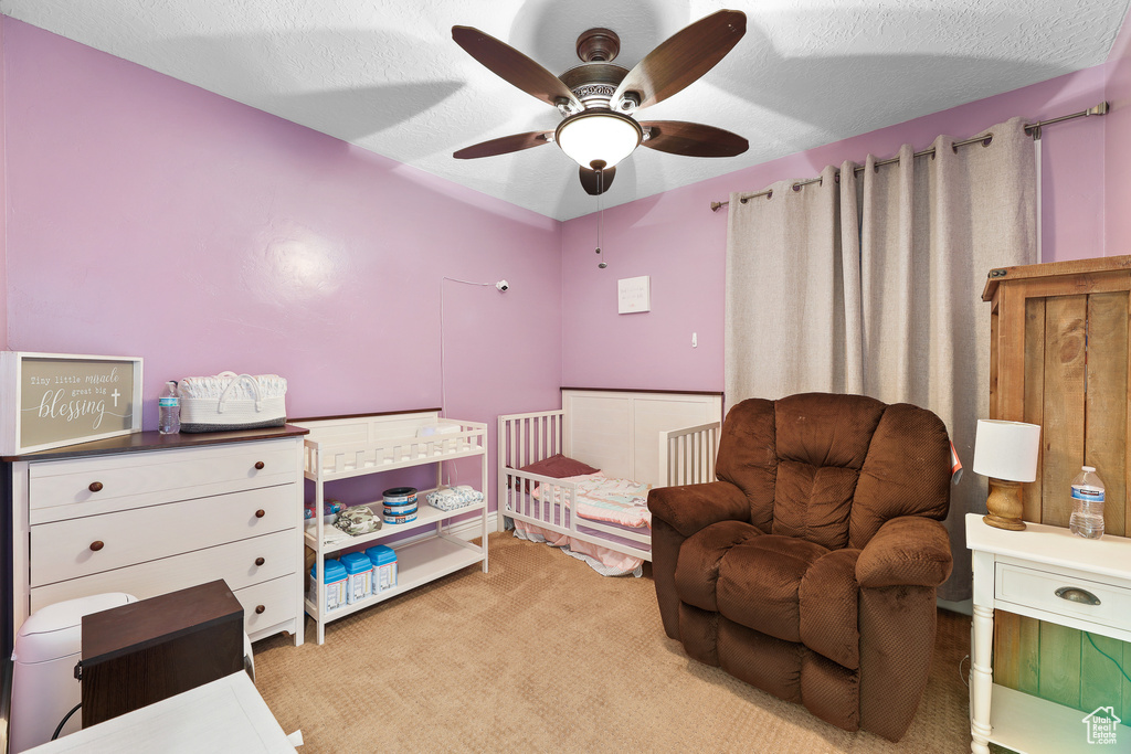 Bedroom with a nursery area, light carpet, a textured ceiling, and ceiling fan