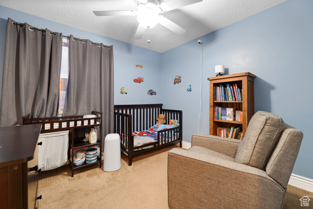 Carpeted bedroom featuring a nursery area, ceiling fan, and a textured ceiling