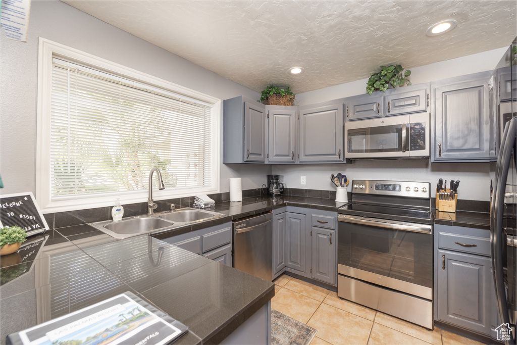 Kitchen featuring light tile flooring, appliances with stainless steel finishes, gray cabinetry, and sink