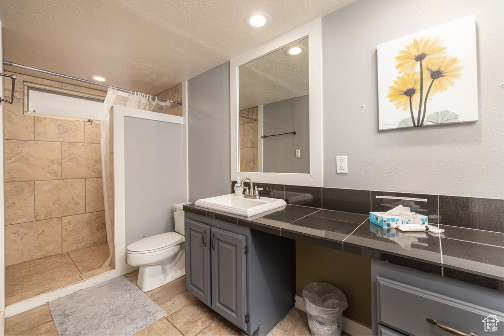 Bathroom featuring a shower with shower curtain, a textured ceiling, toilet, tile floors, and vanity with extensive cabinet space