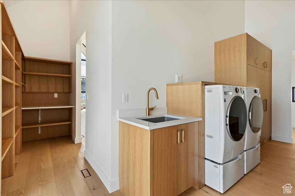 Washroom featuring light hardwood / wood-style floors, independent washer and dryer, cabinets, and sink