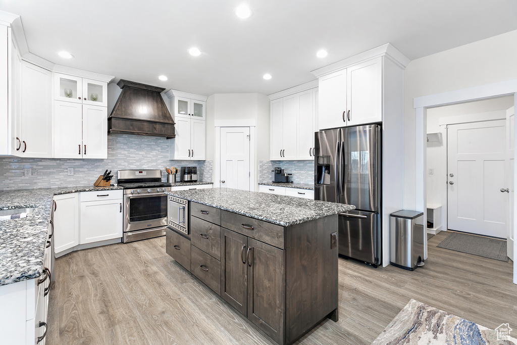 Kitchen featuring premium range hood, backsplash, appliances with stainless steel finishes, light hardwood / wood-style floors, and a center island