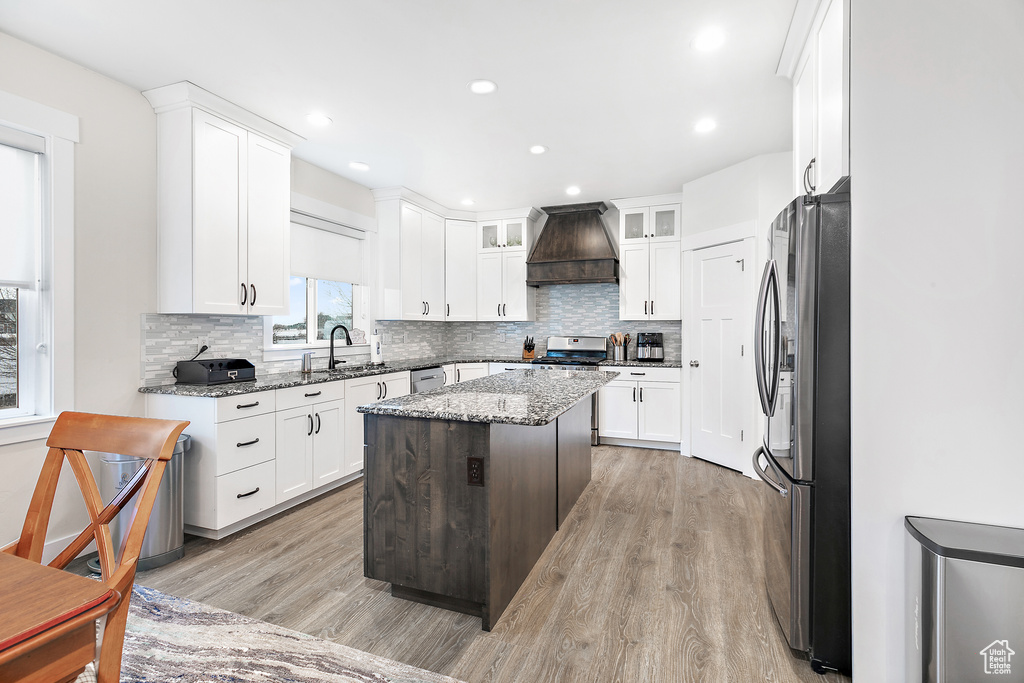 Kitchen featuring premium range hood, light wood-type flooring, stainless steel fridge, and light stone counters