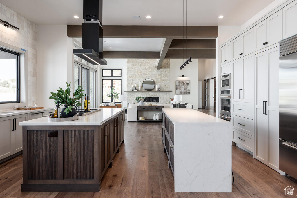 Kitchen with white cabinets, dark hardwood / wood-style floors, appliances with stainless steel finishes, and a kitchen island