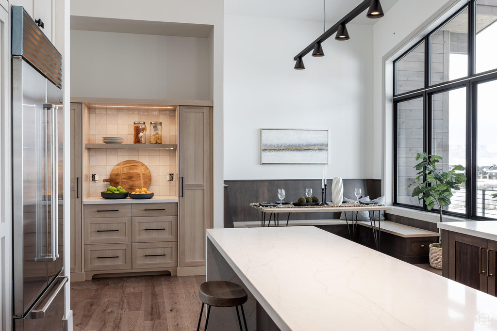 Kitchen featuring dark wood-type flooring, light stone countertops, a kitchen breakfast bar, built in fridge, and track lighting
