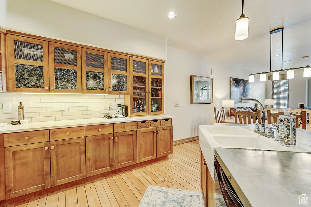 Kitchen with light hardwood / wood-style flooring, decorative light fixtures, backsplash, and sink