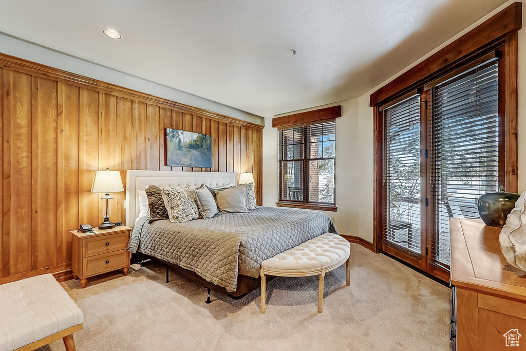 Bedroom with multiple windows, access to exterior, wooden walls, and light carpet