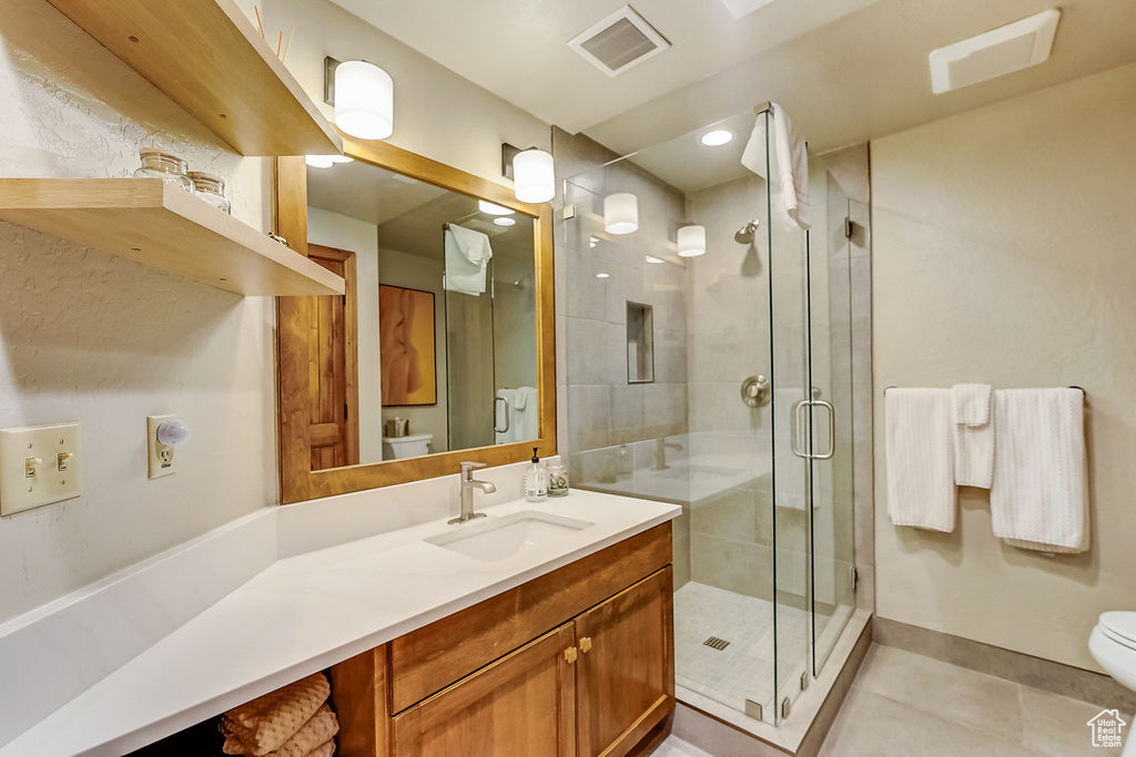 Bathroom featuring toilet, a shower with door, tile floors, and vanity with extensive cabinet space