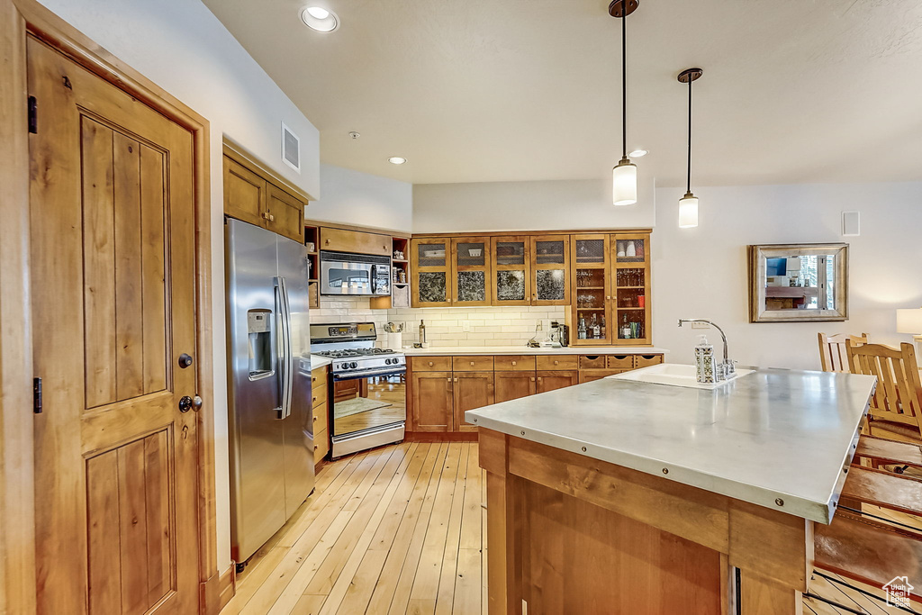 Kitchen with pendant lighting, stainless steel appliances, backsplash, light hardwood / wood-style floors, and sink