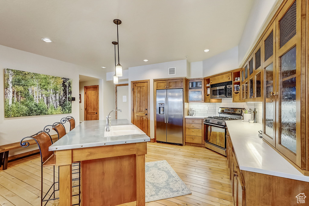 Kitchen featuring hanging light fixtures, appliances with stainless steel finishes, light hardwood / wood-style flooring, and a kitchen breakfast bar