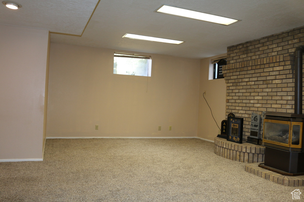 Basement featuring brick wall, light carpet, and a wood stove