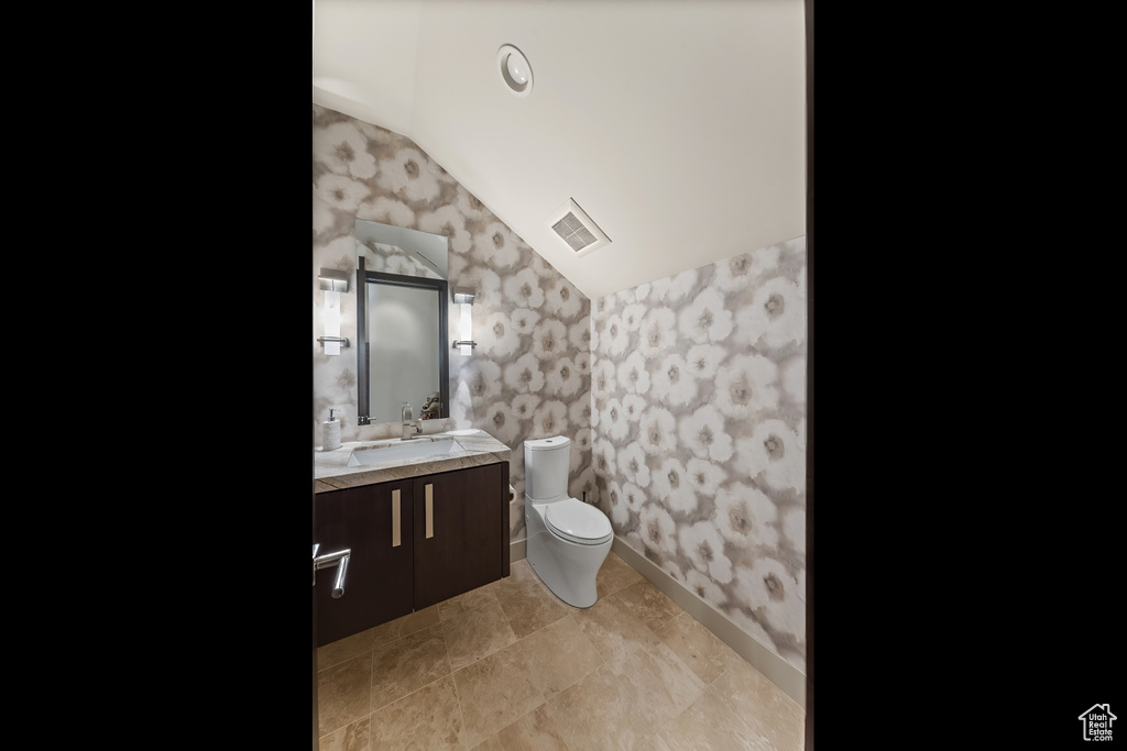 Bathroom with vaulted ceiling, vanity, tile flooring, and toilet