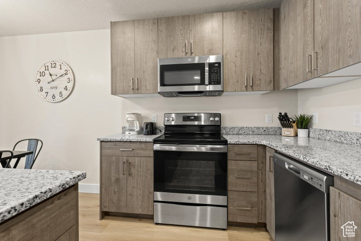 Kitchen featuring appliances with stainless steel finishes, light stone counters, and light wood-type flooring