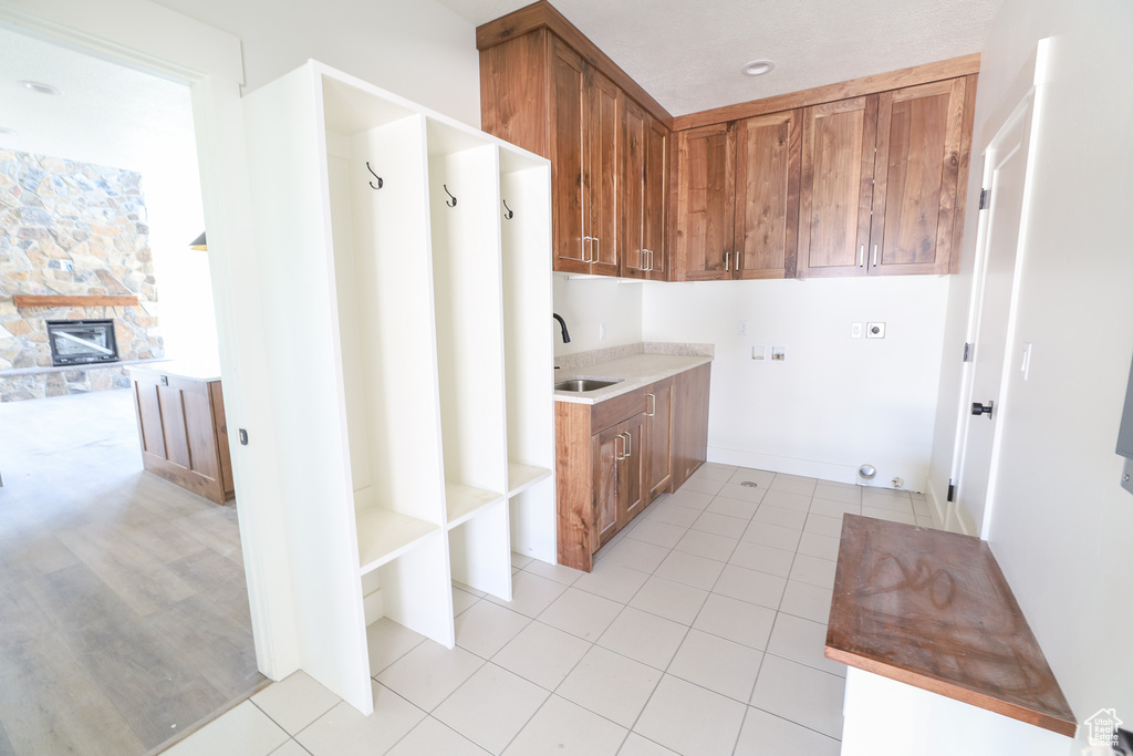 Laundry area with electric dryer hookup, a stone fireplace, light hardwood / wood-style floors, sink, and cabinets