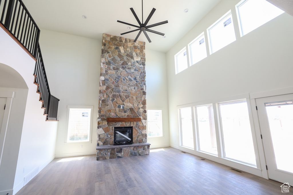 Unfurnished living room featuring ceiling fan, a towering ceiling, hardwood / wood-style flooring, and a stone fireplace