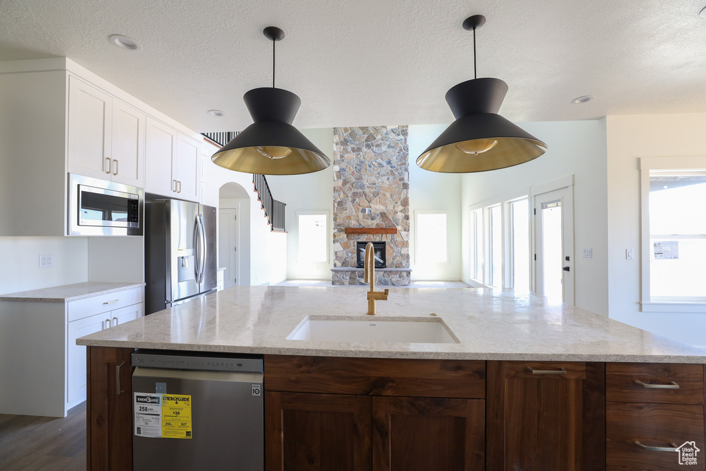 Kitchen featuring pendant lighting, white cabinets, a fireplace, appliances with stainless steel finishes, and a kitchen island with sink