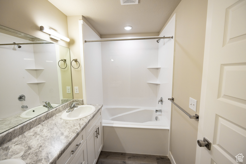 Bathroom featuring wood-type flooring, shower / washtub combination, and dual vanity