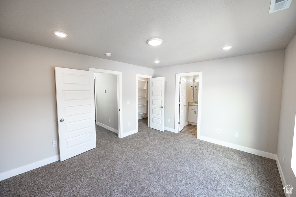 Unfurnished bedroom with connected bathroom, a closet, a spacious closet, and light carpet