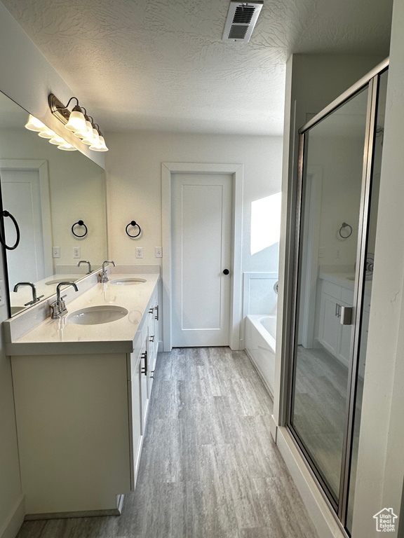 Bathroom with a textured ceiling, hardwood / wood-style floors, double sink, large vanity, and separate shower and tub