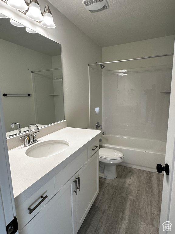 Full bathroom with vanity, a textured ceiling, toilet, tub / shower combination, and wood-type flooring