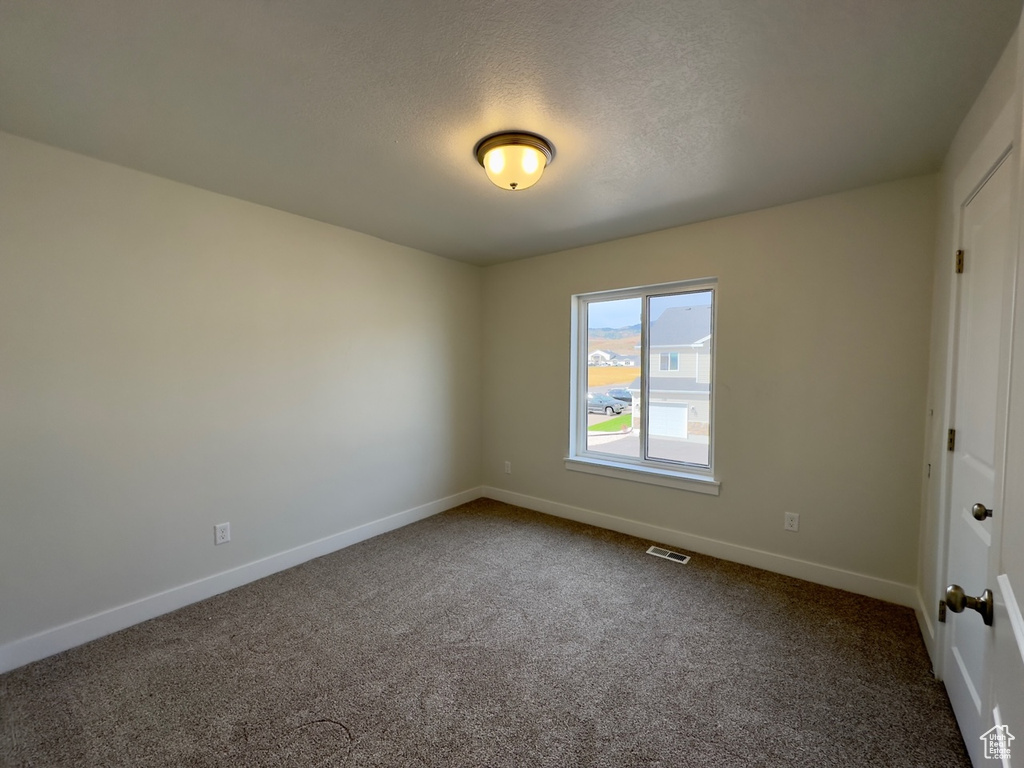 Empty room with dark colored carpet and a textured ceiling