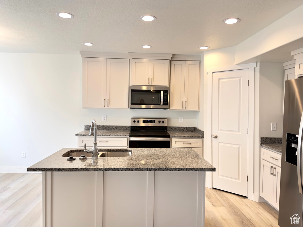 Kitchen featuring light hardwood / wood-style flooring, white cabinets, dark stone counters, sink, and stainless steel appliances