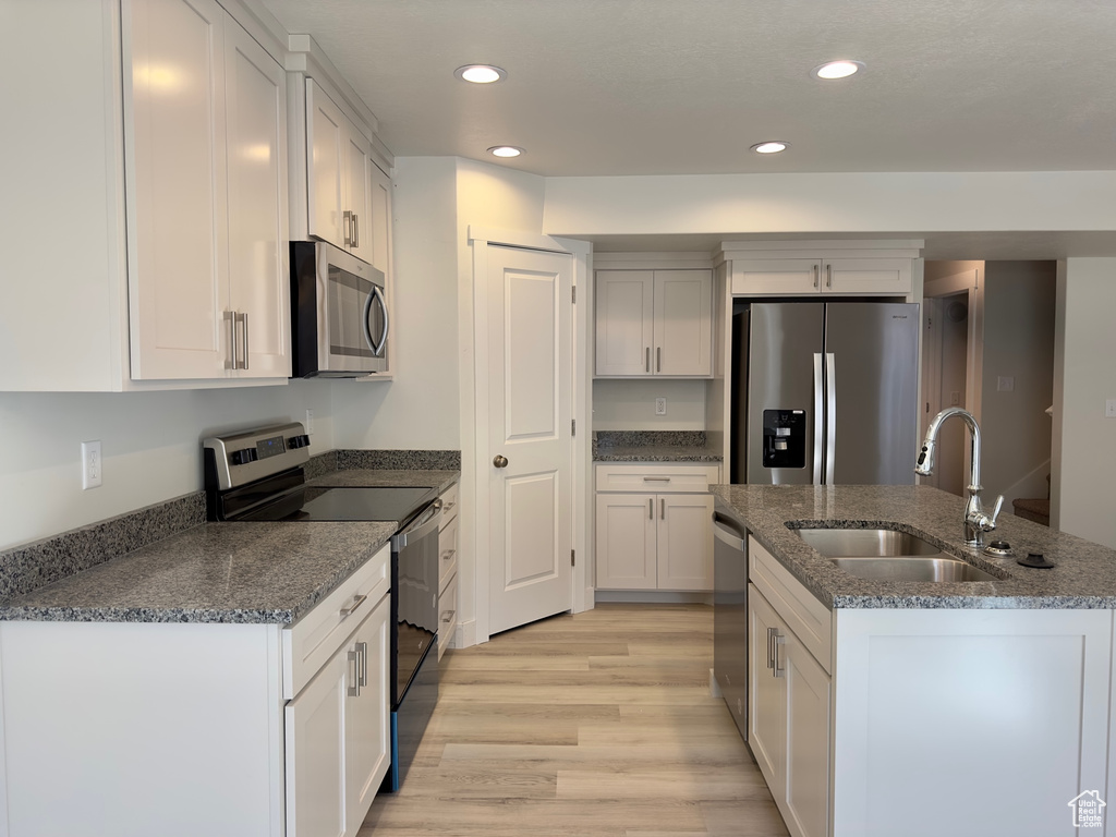 Kitchen with white cabinets, appliances with stainless steel finishes, light wood-type flooring, and sink