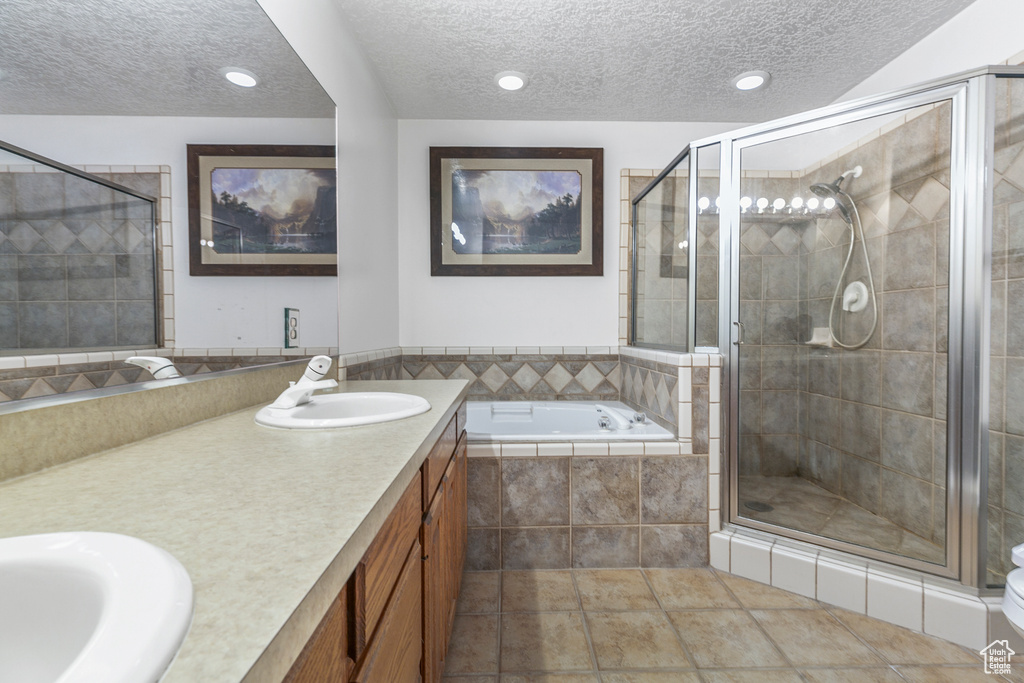 Bathroom featuring a textured ceiling, vanity with extensive cabinet space, double sink, independent shower and bath, and tile flooring